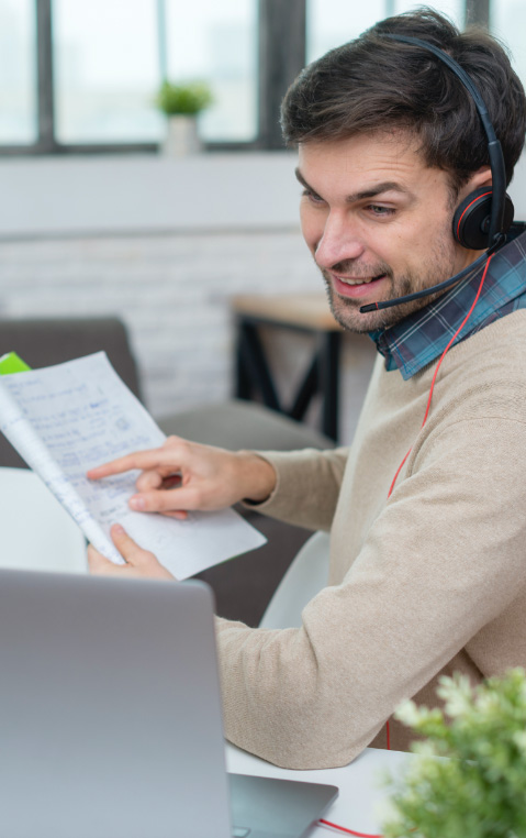 A person sitting with a notebook in hand, a computer at his side and talking to a headset